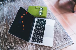 From above composition of opened laptop with keyboard and green closed notebook with glasses placed on wooden table in Thailand